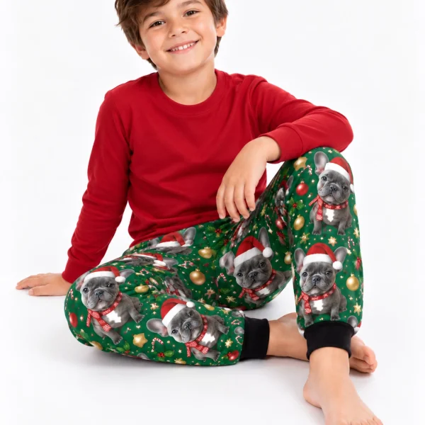 Boy sitting in kids Christmas pajama pants covered in French bulldog faces in Santa hats and scarves — MyDogPics