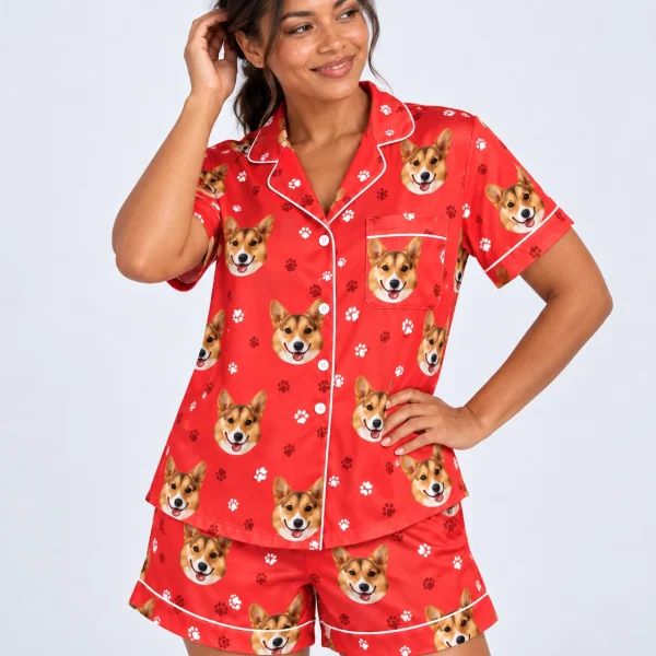 Woman wearing a satin pajamas for women covered in tan-and-white corgi faces on red paw-print satin — MyDogPics