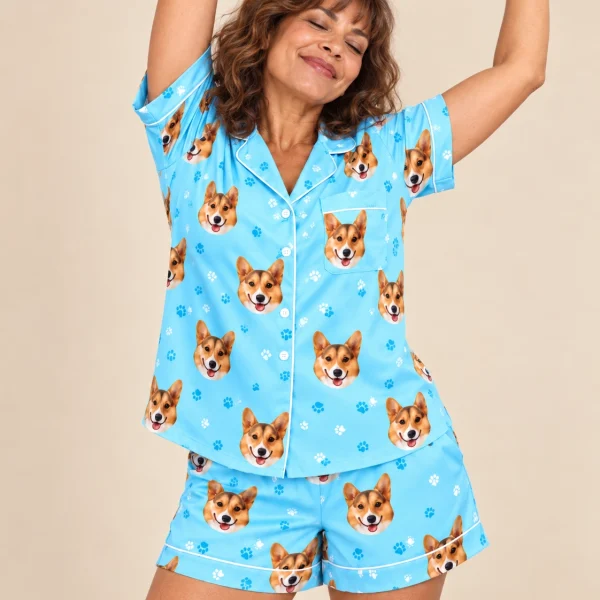 Woman posing in a short pajama set, tan-and-white corgi faces on light blue paw-print satin — MyDogPics