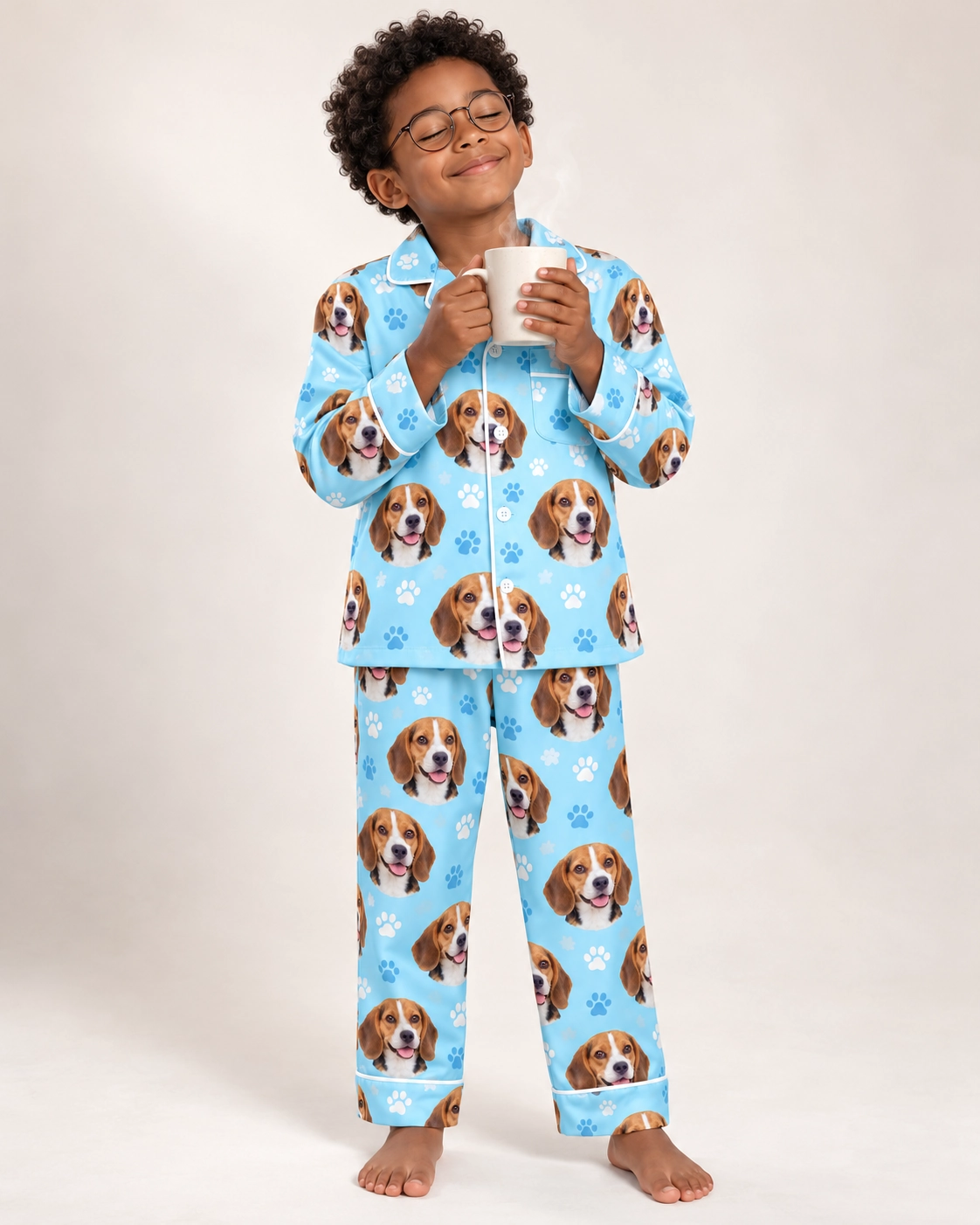 Kids Beagle Pajamas – Front View, Light Blue Paw-Print | MyDogPics Boy wearing kids beagle pajamas covered in tricolor Beagle (black, tan and white) faces — MyDogPics