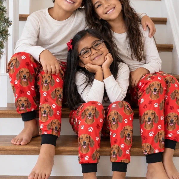 Kids in matching kids dachshund pajama pants with red smooth-coated Dachshund faces on red paw-print fabric — MyDogPics
