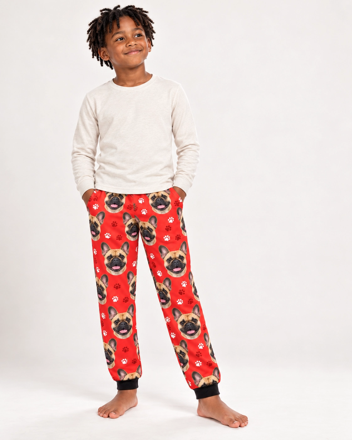 Kids French Bulldog Pajama Pants – Front View, Red Paw-Print | MyDogPics Boy wearing kids French bulldog pajama pants covered in fawn French Bulldog faces on red paw-print fabric — MyDogPics