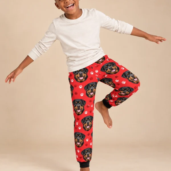 Boy posing in kids rottweiler pajama pants, black-and-mahogany Rottweiler faces on red paw-print fabric — MyDogPics