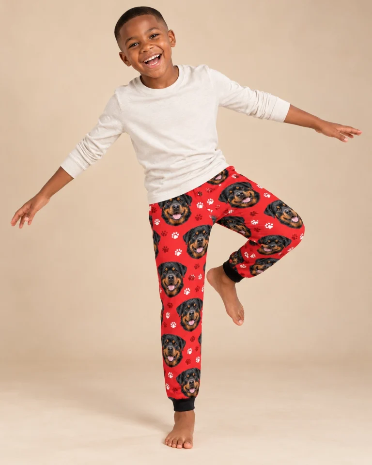 Boy posing in kids rottweiler pajama pants, black-and-mahogany Rottweiler faces on red paw-print fabric — MyDogPics